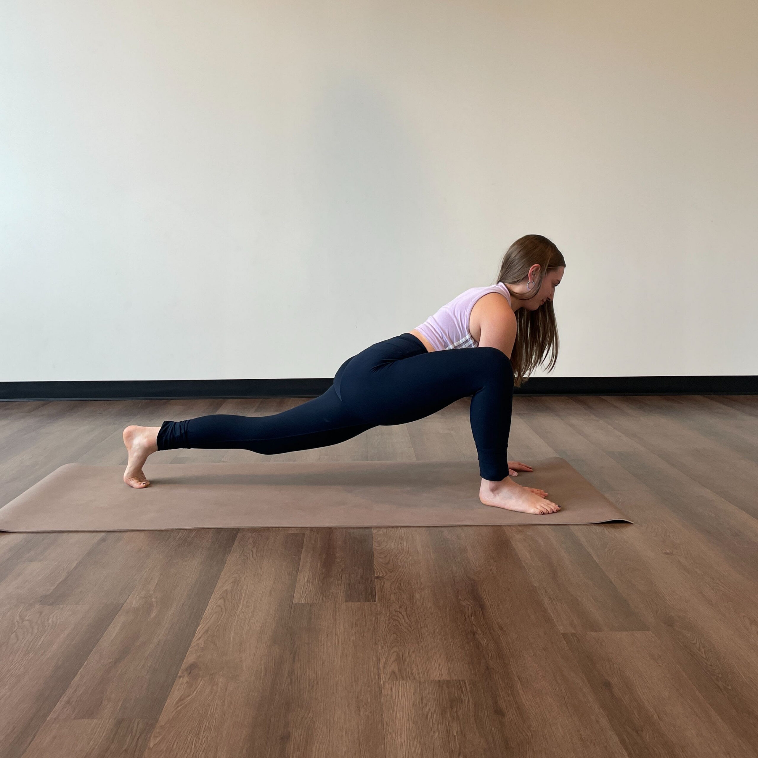 Zoe Lowden, a white woman with long brown hair wearing black leggings and a light purple tank top practices utthan pristasana.