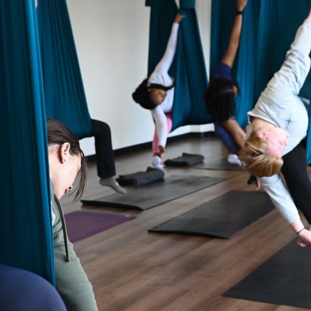 A group of women attend an aerial yoga class.